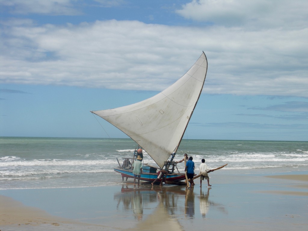 3 men prepare to launch a jangada from the beach. 