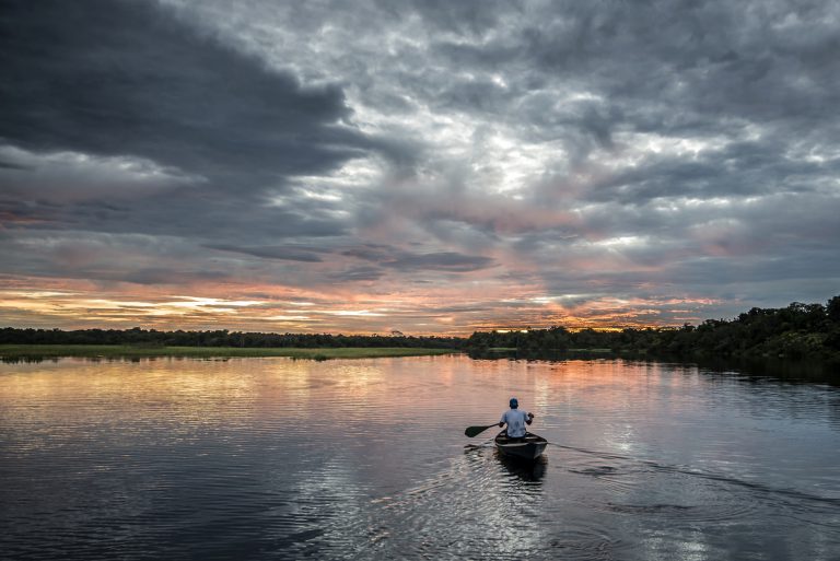 A man paddles his piroque into the sunset. 