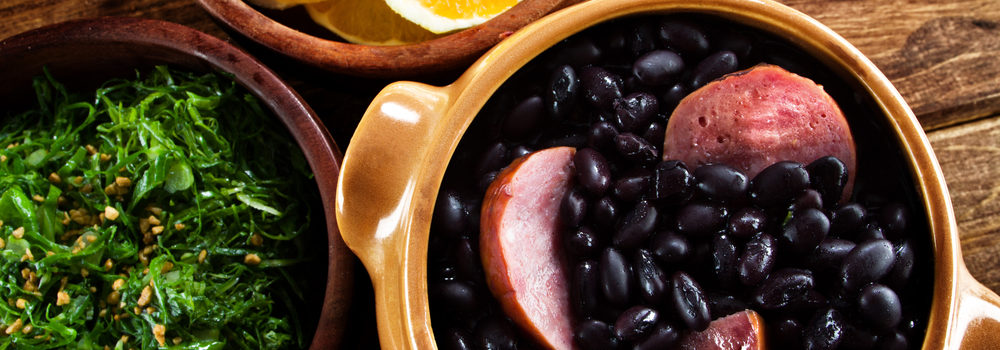 Feijoada with a dish of orange slices and kale.