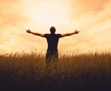 Man raises his hands and looks at the sunset.