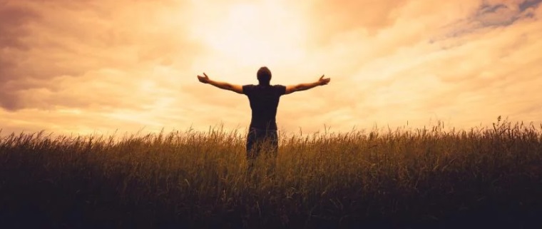 Man raises his hands and looks at the sunset.